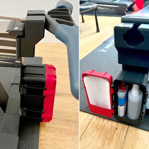 May include: A black and red storage box attached to a Concept2 rowing machine. The box is open, revealing a roll of white paper towels and two bottles of cleaning solution. The rowing machine has a gray handle.