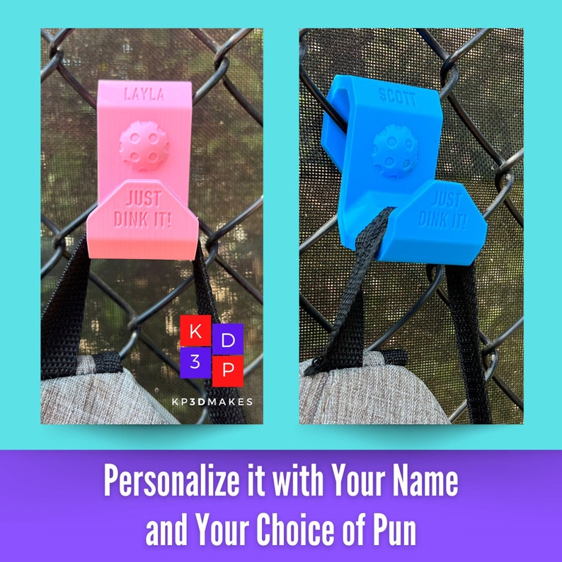 Op de afbeelding: Roze en blauwe pickleball-tas haken met de tekst "LAYLA" en "SCOTT" erop gedrukt. Elke haak heeft de tekst "JUST DINK IT!" en een pickleball-ontwerp. De haken zijn bevestigd aan een hek van gaas.