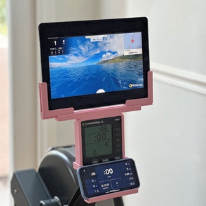 May include: A pink and black rowing machine with a digital display showing the time, distance, and strokes per minute. The machine has a tablet holder with a screen displaying a map and the words "Kinomap".
