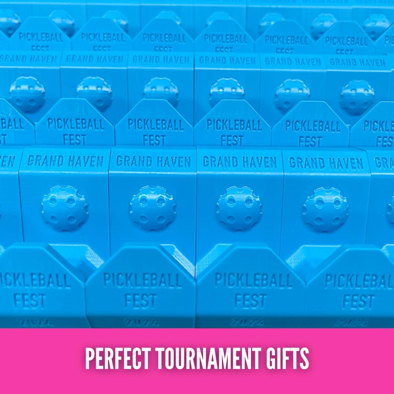 Op de afbeelding: Close-up van meerdere blauwe pickleball-items. Elk item heeft de tekst "PICKLEBALL FEST GRAND HAVEN" erop gedrukt. De tekst "PERFECT TOURNAMENT GIFTS" staat onderaan de afbeelding.