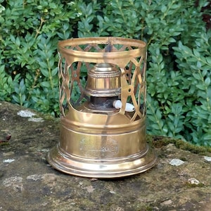 May include: Brass camping stove with a decorative cage and a white knob. The stove has a label that reads "The Best Made".