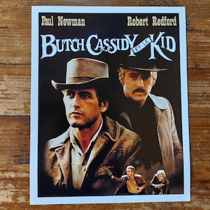 Peut inclure: Une affiche de film vintage pour le film "Butch Cassidy et le Kid" avec Paul Newman et Robert Redford. L'affiche présente un gros plan des deux acteurs dans leurs chapeaux de cow-boy et leurs tenues iconiques.