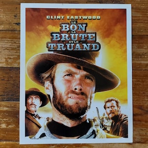 Peut inclure: Affiche de film avec Clint Eastwood portant un chapeau de cowboy. Le titre du film est "Le Bon, La Brute et le Truand". L'affiche a un fond jaune et orange.