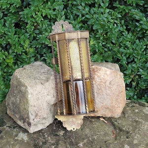 以下が含まれることがあります： 装飾的なデザインとガラス容器が付いた金色の金属製のオイルランプ。ランプは岩の上に置かれています