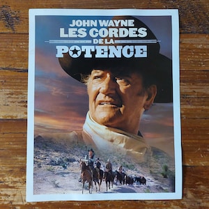 Peut inclure: Affiche de film vintage mettant en scène John Wayne portant un chapeau de cowboy. L'affiche est pour le film "Les Cordes de la Potence" et présente un arrière-plan de coucher de soleil avec un groupe de cowboys à cheval.