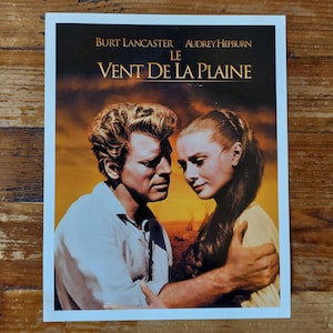 Peut inclure: Une affiche de film vintage mettant en scène Burt Lancaster et Audrey Hepburn dans une étreinte romantique. L'affiche est pour le film "Le Vent de la Plaine" et présente un fond de coucher de soleil.