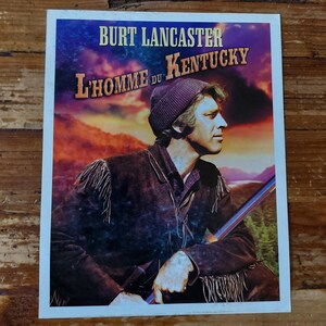 Peut inclure: Une affiche de film vintage mettant en scène Burt Lancaster dans une pose rustique et en plein air. L'affiche est pour le film "L'homme du Kentucky" et présente un arrière-plan de coucher de soleil avec un lac au loin.
