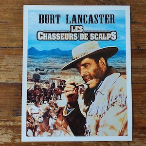 Peut inclure: Affiche de film vintage mettant en scène Burt Lancaster portant un chapeau de cowboy et fumant une pipe. L'affiche est pour le film "Les Chasseurs de Scalps" et a un fond de ciel bleu et de paysage désertique.