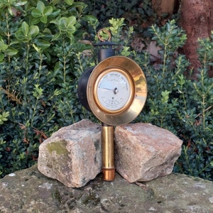 May include: A brass and black weather instrument with a round face and a long brass stem. The face has a white background with black markings and the text "ALTIMETRE VARIABLE BAROMETRE".
