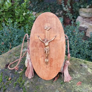 Peut inclure: Une boîte en bois de forme ovale avec un petit crucifix en or et une figurine de Jésus-Christ. La boîte a une poignée en corde brune avec des glands à chaque extrémité.