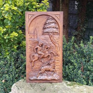 May include: A wooden wall plaque with a carved scene of a knight on horseback chasing a wild boar. The plaque is set against a backdrop of a forest with a castle in the distance.