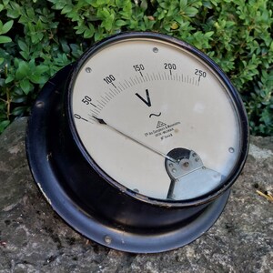 Può includere: Un voltmetro vintage in bianco e nero con un ago curvo. L'indicatore legge fino a 250 volt, con segni a 50, 100, 150 e 200. Il quadrante include il testo "Cr. des Compteurs & Manomètres LIEGE - BELGIQUE N° 10446".