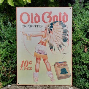 Può includere: Cartello in metallo vintage Old Gold Cigarettes. Il cartello presenta un'illustrazione di una donna in abiti nativi americani con arco e frecce. Il cartello recita "Old Gold Cigarettes" e "10¢ A PACK".