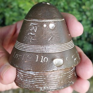 Peut inclure: Objet conique de couleur bronze avec un sommet arrondi et une base striée. L'objet présente des rayures horizontales blanches et des marquages gravés, dont le numéro "110" et le texte "Lot No".
