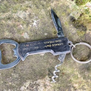 Peut inclure: Un porte-clés multi-outils noir avec un ouvre-bouteille, un tire-bouchon et un petit couteau. Le porte-clés porte l'inscription "GARAGE CHM... 19340 PREAUX".