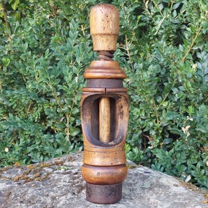 Op de afbeelding: Een vintage houten kurkentrekker met een cilindrisch handvat, een centrale verticale schacht en een donker metalen ringmechanisme. Het hout vertoont een natuurlijke nerf met zichtbare slijtage, kleine deukjes en een verweerde afwerking.