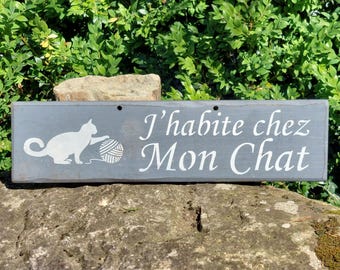 Puede incluir: Un letrero de madera gris con texto blanco y un dibujo de un gato. El letrero dice "J'habite chez Mon Chat", con un gato jugando con una bola de lana. El letrero se muestra al aire libre.