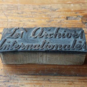 May include: A vintage wood printing block with the text "Les Archives Internationales" in raised letters.