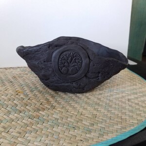 May include: A black ceramic bowl with a tree of life design. The bowl has a rough, textured surface and is shaped like a crescent moon.