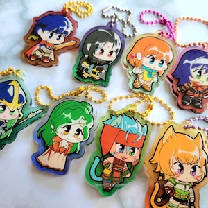 May include: A collection of colorful acrylic keychains featuring anime-style characters. Each keychain has a unique character design with vibrant colors and attached to a gold or silver chain. The keychains are ideal for fans of anime or manga.