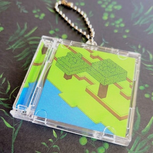 May include: A clear plastic keychain with a small, colorful image of a pixelated landscape with two trees. The image is set in a clear plastic case with a silver chain.