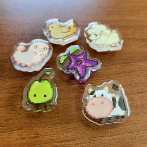 Six shoe charms sitting on a desk. The six shoe charms are: Silk worm, junimo, chicken, sheep, stardop, and cow