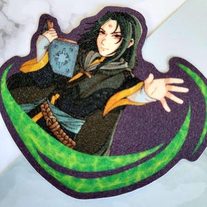 May include: A sticker featuring a stylized illustration of a character with long green hair, red eyes, and a dark cloak. The character holds a blue book with a star design and is surrounded by a green, swirling design against a purple background.