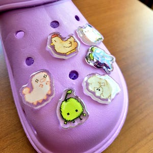 Six shoe charms sitting on a purple shoe. The six shoe charms are: Silk worm, junimo, chicken, sheep, stardop, and cow