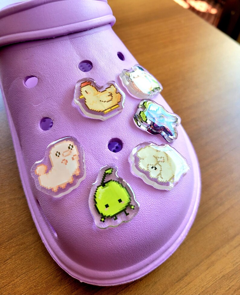 Six shoe charms sitting on a purple shoe. The six shoe charms are: Silk worm, junimo, chicken, sheep, stardop, and cow