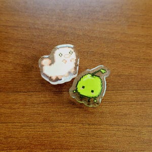 Two shoe charms sitting on a desk. The two charms are silk worm and junimo