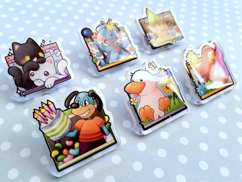 May include: A collection of seven clear acrylic pins featuring cartoon animal characters. The pins include a black cat, a blue elephant, a person in a green hat, a pink penguin, a duck, and a dog holding a cake. The background is a light blue surface with white polka dots.