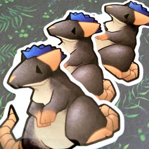 May include: Three stickers featuring a cartoon rat with a blue mohawk, orange ears and paws, and a tan tail. The rat is primarily gray and black, with a white border. The stickers are on a dark green background with a leaf pattern.