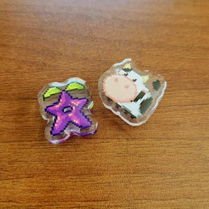 Two shoe charms sitting on a desk. The two charms are stardrop and cow