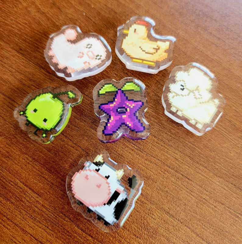 Six shoe charms sitting on a desk. The six shoe charms are: Silk worm, junimo, chicken, sheep, stardop, and cow