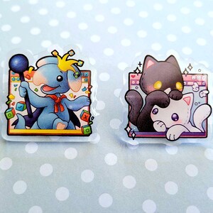 May include: Two clear stickers with cartoon illustrations. One features a blue elephant-like character with a staff and crown. The other shows a black cat and a white cat. Both stickers have a decorative border.