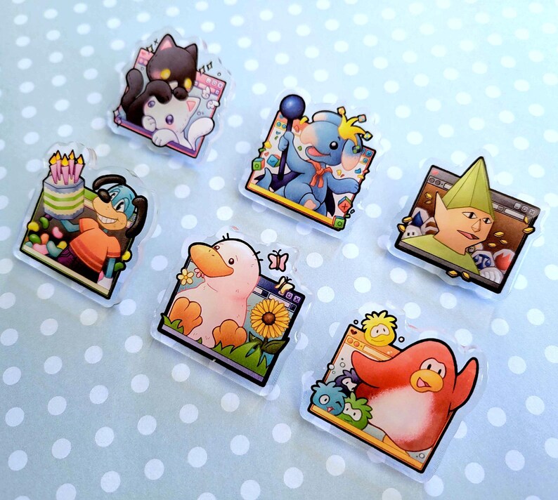 May include: A collection of colorful, cartoon-style acrylic pins featuring various characters. Designs include a black cat on a white cat, a blue dog with a birthday cake, a blue elephant-like creature, a duck with a sunflower, a green-hatted character, and a red penguin.