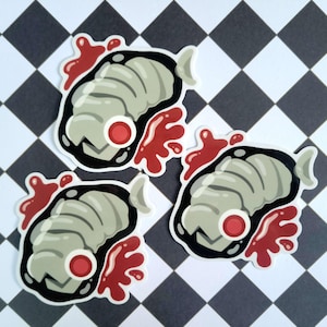 May include: Three stickers featuring a cartoon steak design with a gray, ridged texture, a red circular detail, and a red splash of 'blood'. The stickers have a black outline and a white border, set against a black and white checkered background.