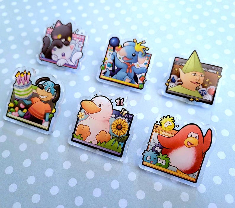 May include: A collection of six clear acrylic pins featuring cartoon characters. The pins showcase a variety of designs, including a black cat and white cat, a blue creature with a staff, a green elf, a dog with a cake, a duck with a sunflower, and a red penguin.
