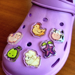 Six shoe charms sitting on a purple shoe. The six shoe charms are: Silk worm, junimo, chicken, sheep, stardop, and cow