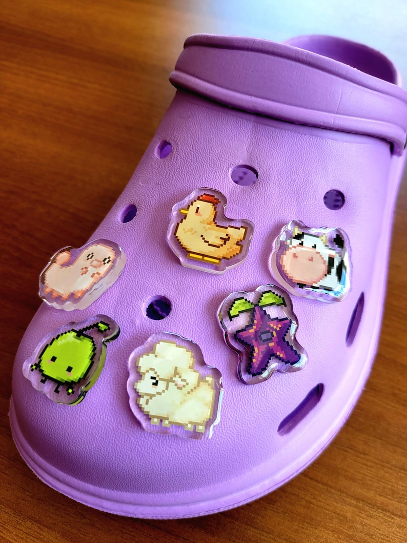 Six shoe charms sitting on a purple shoe. The six shoe charms are: Silk worm, junimo, chicken, sheep, stardop, and cow