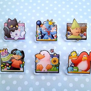 May include: Set of six clear acrylic pins featuring cartoon characters. Designs include a black cat and white cat, a blue elephant with a crown, a green elf, a dog with a cake, a pink duck, and a red penguin. Each pin has a unique background.