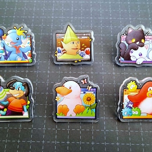 May include: A collection of six clear acrylic pins featuring cartoon characters. The pins showcase a blue elephant with a balloon, a yellow-green elf, a black cat with a white cat, a dog with a cake, a duck with a sunflower, and a red penguin.