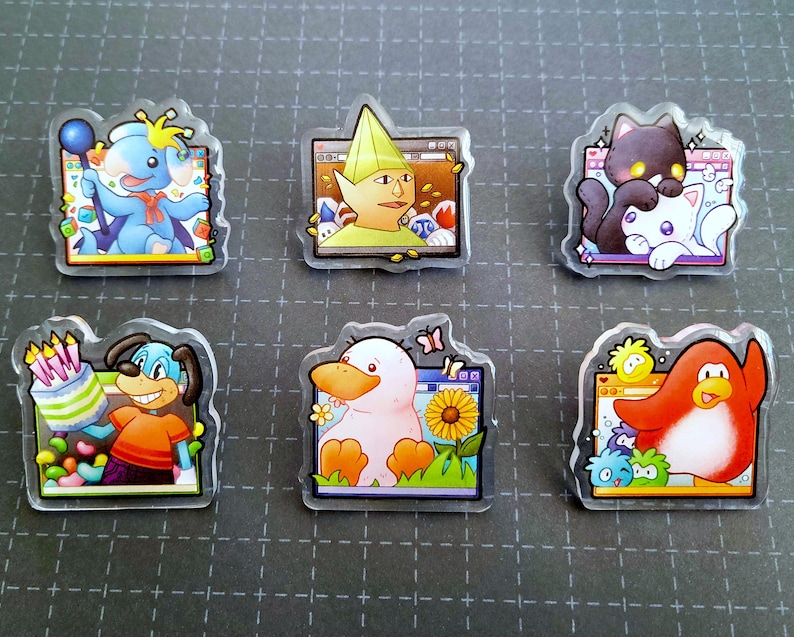 May include: A collection of six clear acrylic pins featuring cartoon characters. The pins showcase a blue elephant with a balloon, a yellow-green elf, a black cat with a white cat, a dog with a cake, a duck with a sunflower, and a red penguin.