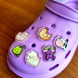 Six shoe charms sitting on a purple shoe. The six shoe charms are: Silk worm, junimo, chicken, sheep, stardop, and cow