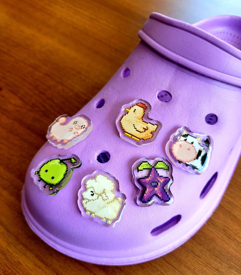 Six shoe charms sitting on a purple shoe. The six shoe charms are: Silk worm, junimo, chicken, sheep, stardop, and cow