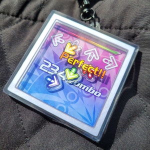 May include: A clear plastic badge holder with a colorful design featuring arrows, the text "Perfect!!" and "23 Combo".
