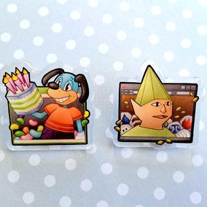 May include: Two clear acrylic pins. One features a cartoon dog holding a birthday cake, the other depicts a character with a green hat in front of a computer screen. The pins have a white border and are on a light blue background with white polka dots.