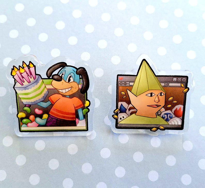 May include: Two clear acrylic pins. One features a cartoon dog holding a birthday cake, the other depicts a character with a green hat in front of a computer screen. The pins have a white border and are on a light blue background with white polka dots.