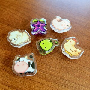 Six shoe charms sitting on a desk. The six shoe charms are: Silk worm, junimo, chicken, sheep, stardop, and cow