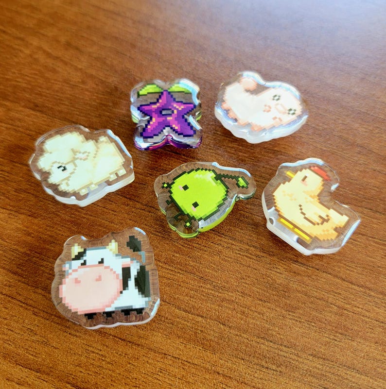 Six shoe charms sitting on a desk. The six shoe charms are: Silk worm, junimo, chicken, sheep, stardop, and cow
